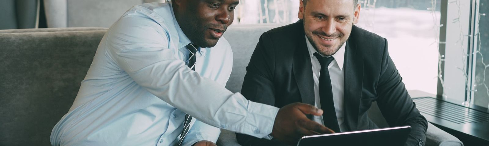 Two businessmen discussing work while using a laptop in a cafe setting.